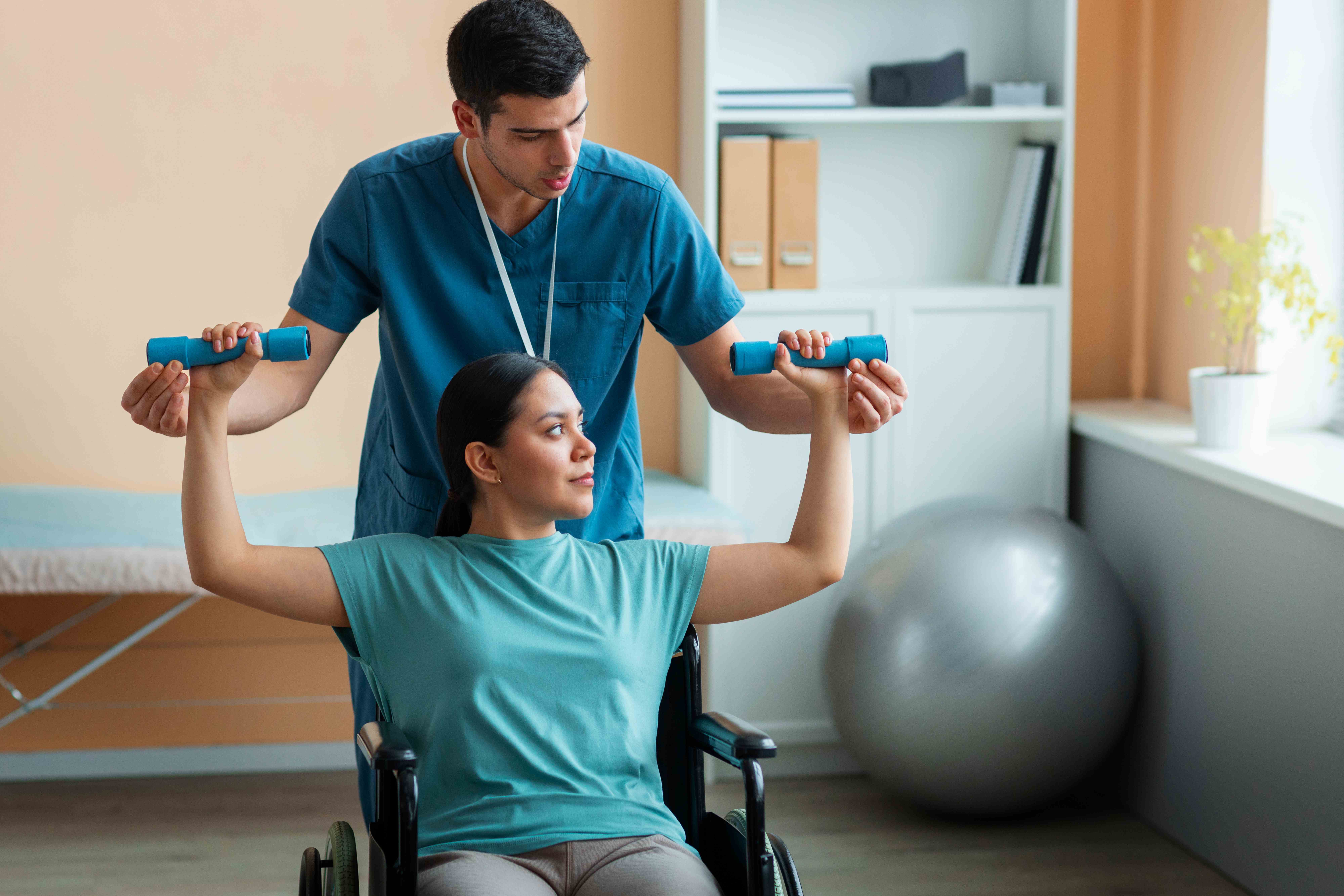 Rehabilitation therapist helping patient in wheelchair with arm exercises
